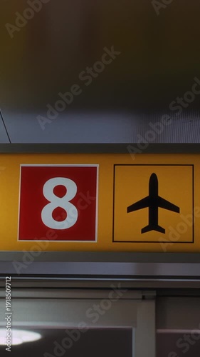 Signage displaying number 8 and airplane icon in a brightly lit airport terminal, indicating boarding gate information for travelers in a modern setting