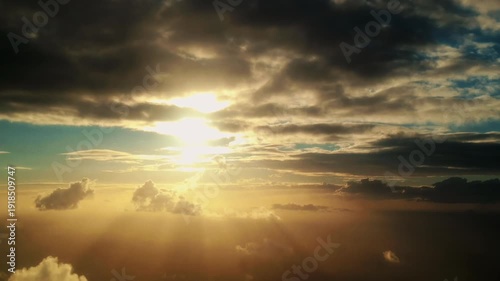 Sunlight breaks through clouds at dawn, illuminating the sky with golden rays and creating a serene atmosphere over the horizon in a breathtaking aerial view