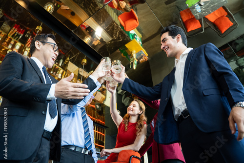Fotografía Diverse team of successful business professionals in formal suits celebrating victory and toasting with glasses during a corporate networking event or happy hour at luxury lounge bar