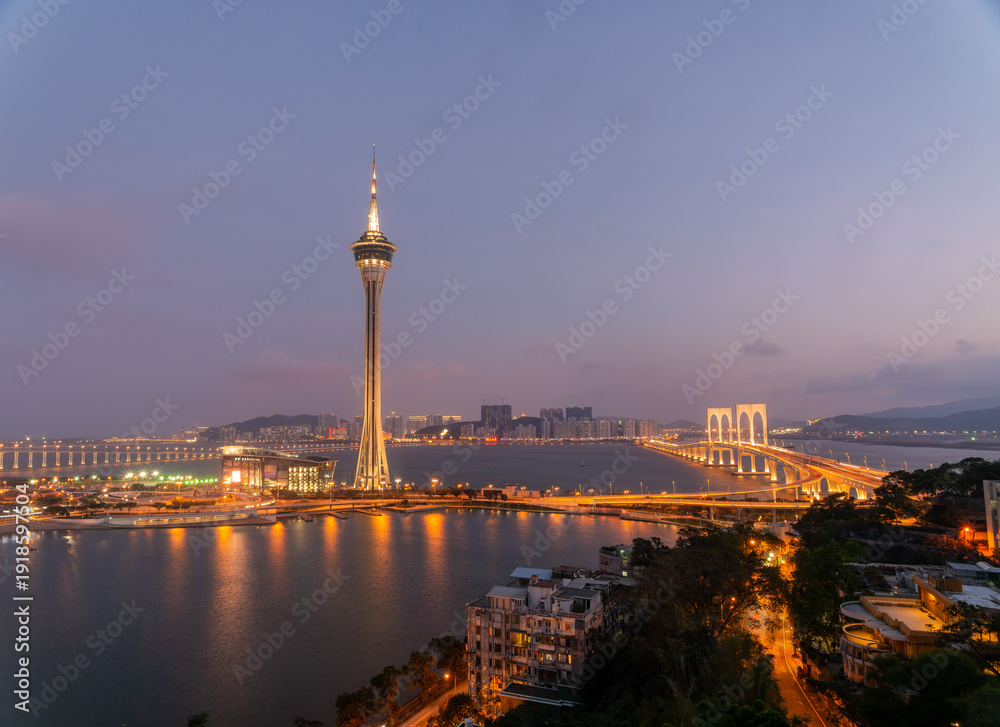 Obraz premium Macau tower and bridges glow at twilight over harbor waters.