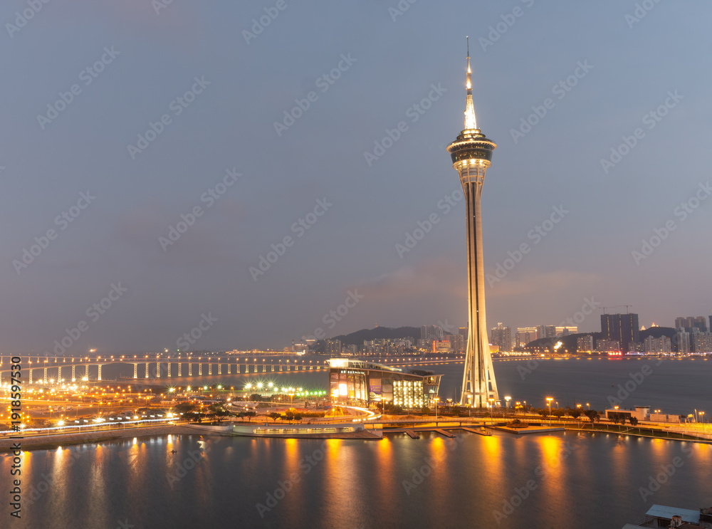 Fototapeta premium Macau tower illuminated at dusk over waterfront cityscape.