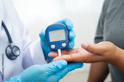 Asian doctor using digital glucose meter for check sample blood sugar level to treatment diabetes.