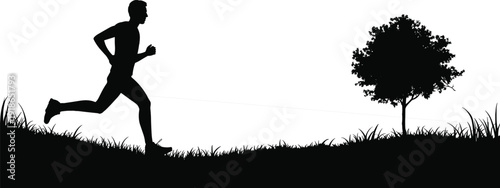 Black silhouette of a male athlete running on a grassy hill next to a small tree during a morning workout in the park