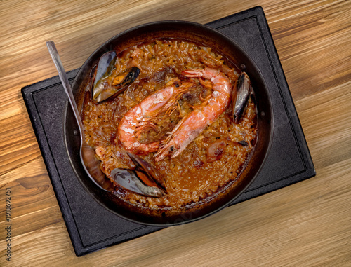 Photography Traditional Spanish seafood paella with large prawns and mussels served in a rustic iron pan on a wooden table