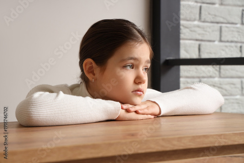 Sad girl at table in room, ...
