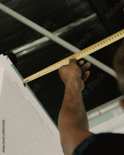 Construction worker measuring drywall panel with tape measure