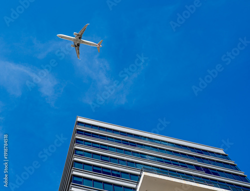 Plane Flyiing over western city.  Bright blue sky with wispy clouds and modern office building.