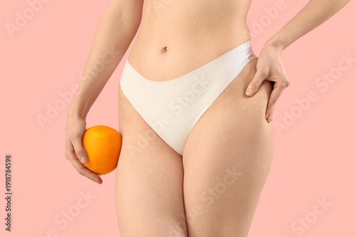 Beautiful young woman in underwear with orange on pink background. Concept of...