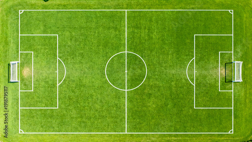 is an aerial view of a rectangular soccer field with a vibrant green grass surface. The field is symmetrically divided by a white center line, with a circular center mark and center circle. Each half 