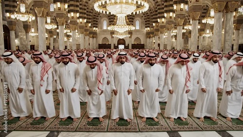 Interior Of Islamic Mosque Filled With People Dressed In White Standing On Floral Designed Green Carpet And Ornate Gold