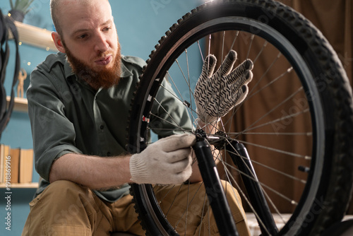 Картината върху платно Portrait of bearded man in shirt repairing and servicing mountain bicycle at home