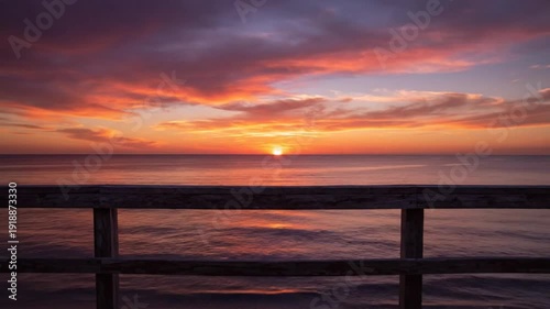 Captivating sunrise over the ocean viewed from a wooden pier with vibrant orange and purple colors in the sky