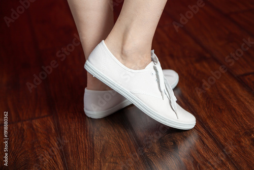 Women legs in white canvas shoes on brown parquet floor