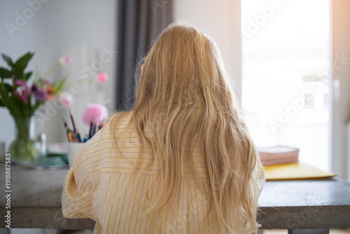 Rear View of Young Girl with Blonde Hair Sitting at a Table