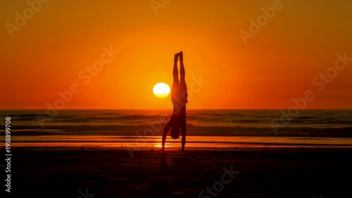 Silhouette of woman practicing yoga on beach at sunset with glowing orange sky and calm ocean horizon