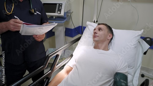 A man lies in a hospital and currently undergoing blood pressure monitoring in a professional medical setting, with a doctor present. 