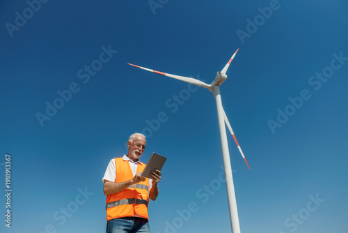 Fotografija Senior male environmentalist inspecting windmill energy with tablet in solar far