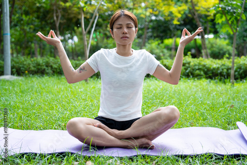 Beautiful young woman practicing Padmasana on yoga mat outdoors, space for text.