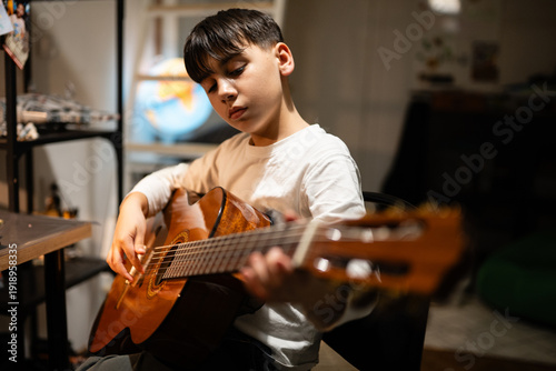 Cuadro en lienzo Young boy practicing playing acoustic guitar at home