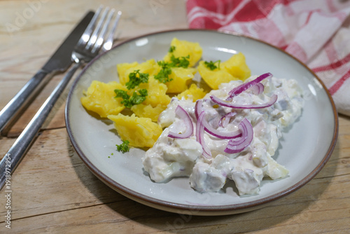 Herring salad in sour cream with red onions, served with jacket potatoes and garnished with parsley on a plate and a rustic wooden table, traditional fish dish in the Netherlands and northern Germany.