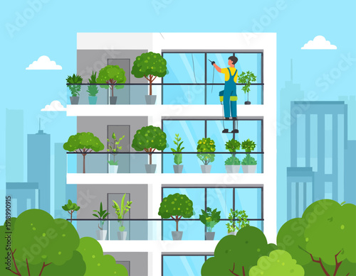 A person on a ladder cleaning windows of a modern apartment building with lush green plants on balconies.