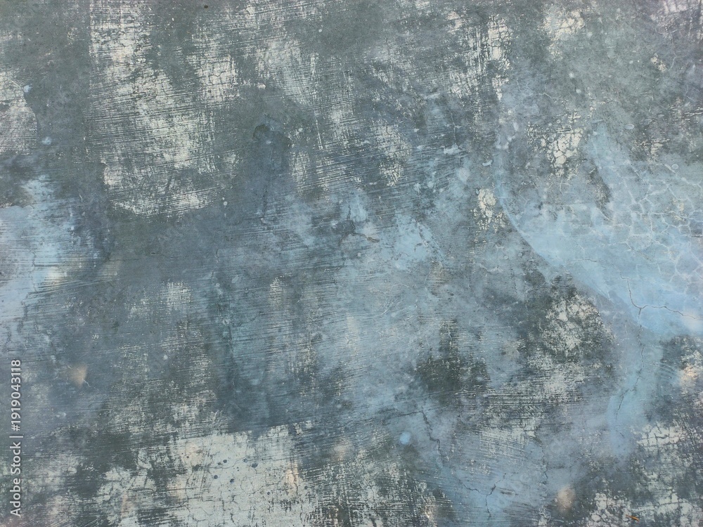 Fototapeta premium A weathered, gray-blue concrete surface featuring heavy textures, faint cracks, mottled white patches, and horizontal brush strokes throughout the frame.