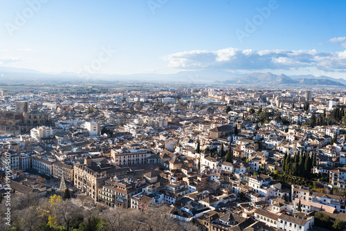 A breathtaking panoramic view of Granada stretching below the majestic Alhambra complex, with snow-capped Sierra Nevada mountains in the distance, showcasing Spain's winter tourism appeal.