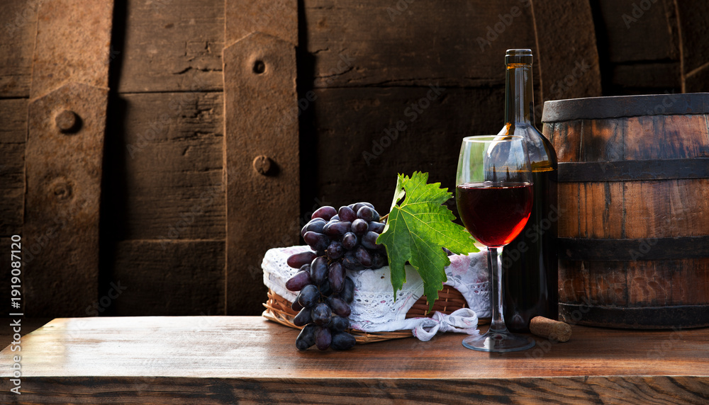 Fototapeta premium Red and white wine bottles with a grape basket on a rustic wooden table, set against a picturesque vineyard landscape. A perfect scene for wine lovers and countryside ambiance. High quality photo