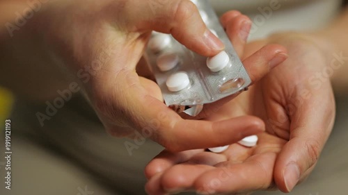 A person carefully removes white pills from a blister pack using one hand, while the other hand holds the pack. This action demonstrates medication preparation