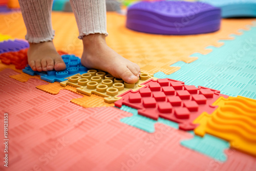 Fotografie Child's bare feet stepping on colorful orthopedic sensory mat puzzles, receiving