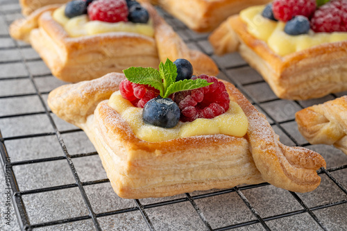 Cuadro en lienzo Danish puff pastry cakes with custard cream and fresh berries, sprinkled with powdered sugar