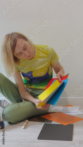 Adult woman in loungewear choosing pastel papers for nostalgic DIY scrapbook at home