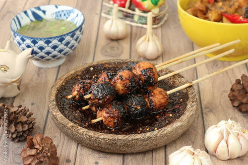 Foto Indonesian food called bakso bakar, or grilled meatballs on skewers, served and seasoned with spicy sweet soy sauce