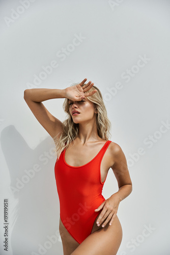 Stunning young woman in a vibrant red swimsuit embracing summer vibes at a stylish backdrop