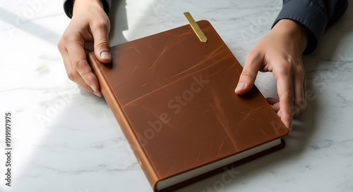 Hands holding brown leather journal on marble desk with gold bookmark