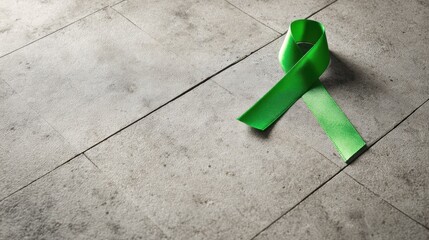 Green awareness ribbon on gray concrete tile background for mental health and environmental campaign, National Donate Life Month