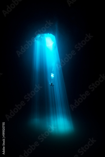 View of a diver suspended in the dark abyss as beams of turquoise light pierce through a cenote, illuminating the underwater cave, Tulum, Quintana Roo, Mexico.