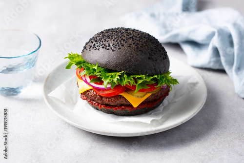 Obraz na plátně Exquisite black bun burger with melted cheese, fresh lettuce, ripe tomato slices, and red onion