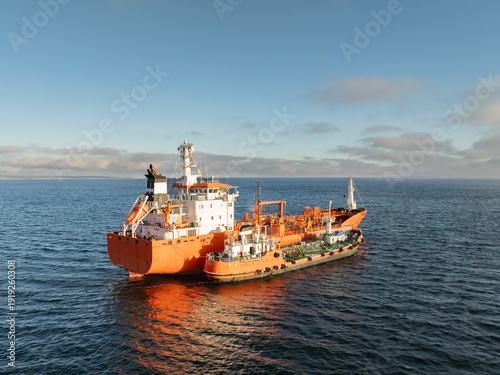 Photos Aerial drone view of orange chemical tanker ship bunkering and refueling from a