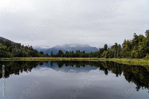 Fotografie Mirror-like lake reflection of snow capped mountains and trees