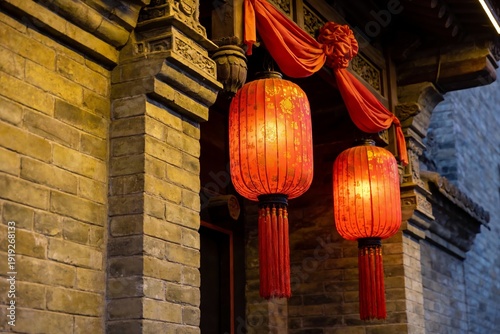 Red lanterns hang from a traditional Chinese building at night, illuminated against stone walls and ornate wooden beams.
