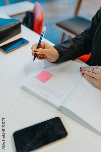 Quadro em tela A person writes in a notebook at a clean desk with a blue pen and a pink sticky note