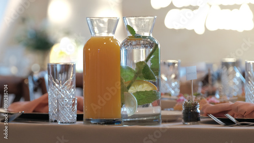 Tablou pe pânză Fresh orange juice and infused water with lemon and mint in glass carafes on a d