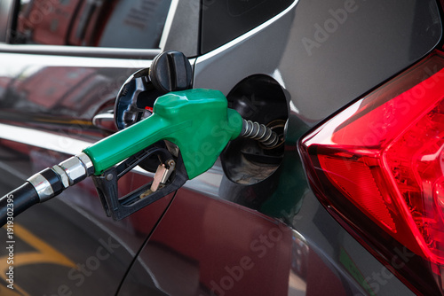 Obraz na plátně Close up of a green fuel nozzle refueling a dark grey car at a gas station