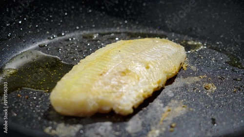 Frying white fish fillets. Frying hake fillets in a hot pan Butter brushed fish fillet in hot pan, closeup of silicone brush glazing fillet with melted butter and oil, gentle. Selective focus