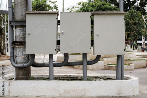 Fotografi Outdoor electrical control boxes mounted on metal post near weathered electric pole in a park