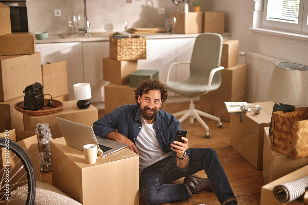 Ταπετσαρία A person sits on the floor surrounded by cardboard boxes in a newly moved-in home while using a laptop and phone, reveling in the thrill of settling in