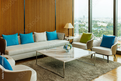 Modern luxury living room interior with a large sofa, colorful pillows, marble coffee table, and wooden lath wall with city view background.