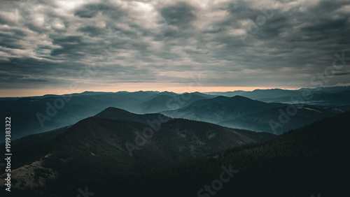 Foto Brooding clouds hang over a chain of shadowed peaks while a thin ribbon of light