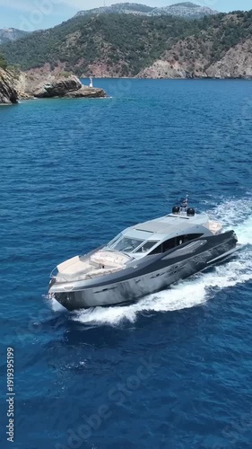 Sleek modern yacht cruising through clear blue ocean waters near a rocky coastline